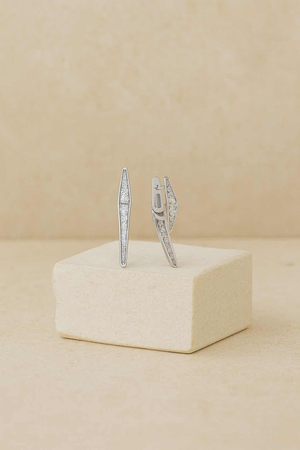 Pair of silver earrings on a beige cube with a beige background