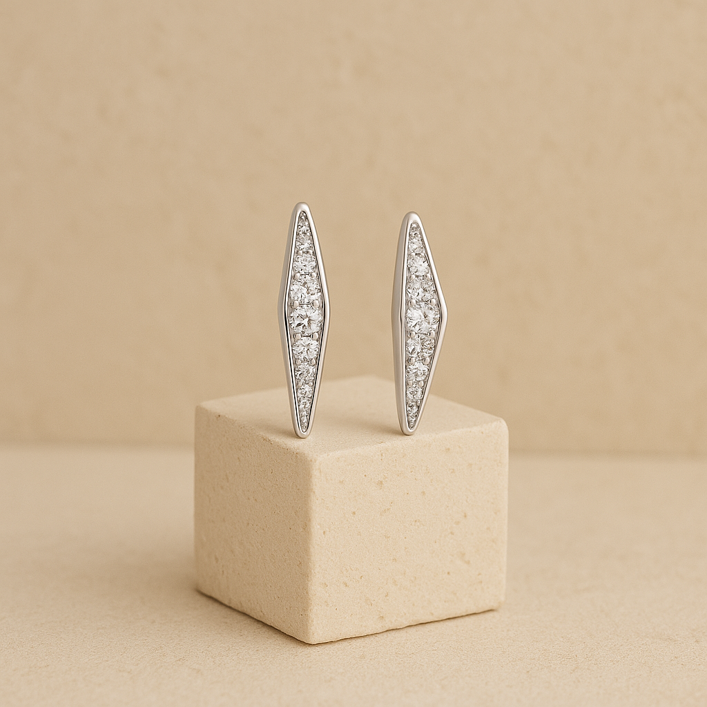Pair of silver earrings with clear stones on a beige cube against a beige background