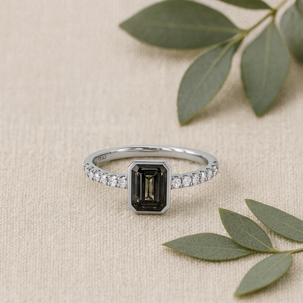 Silver ring with a black gemstone and diamond accents on a beige background with green leaves.