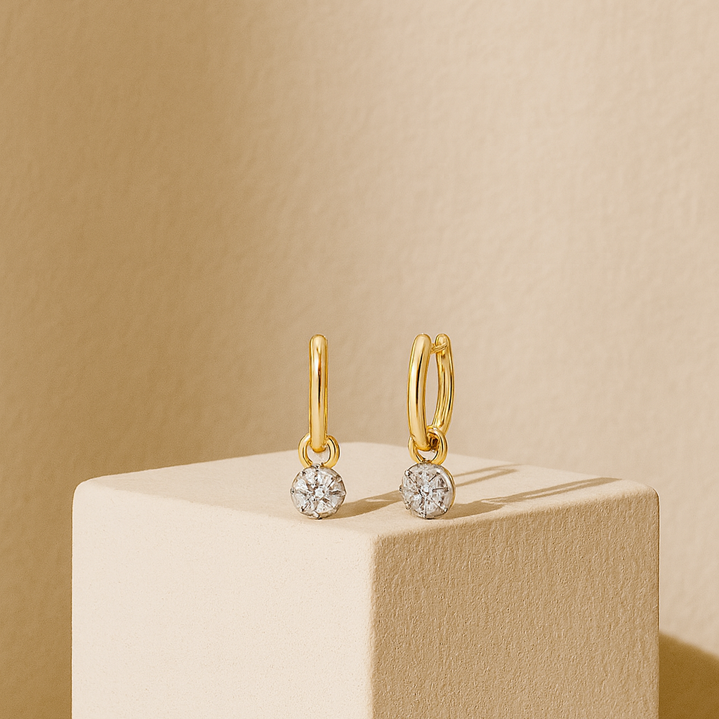 Gold hoop earrings with small round gemstones on a beige cube against a beige background