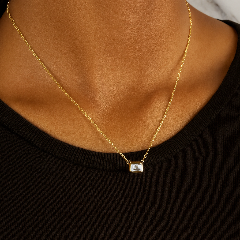 Gold necklace with a small pendant on a person wearing a black top.
