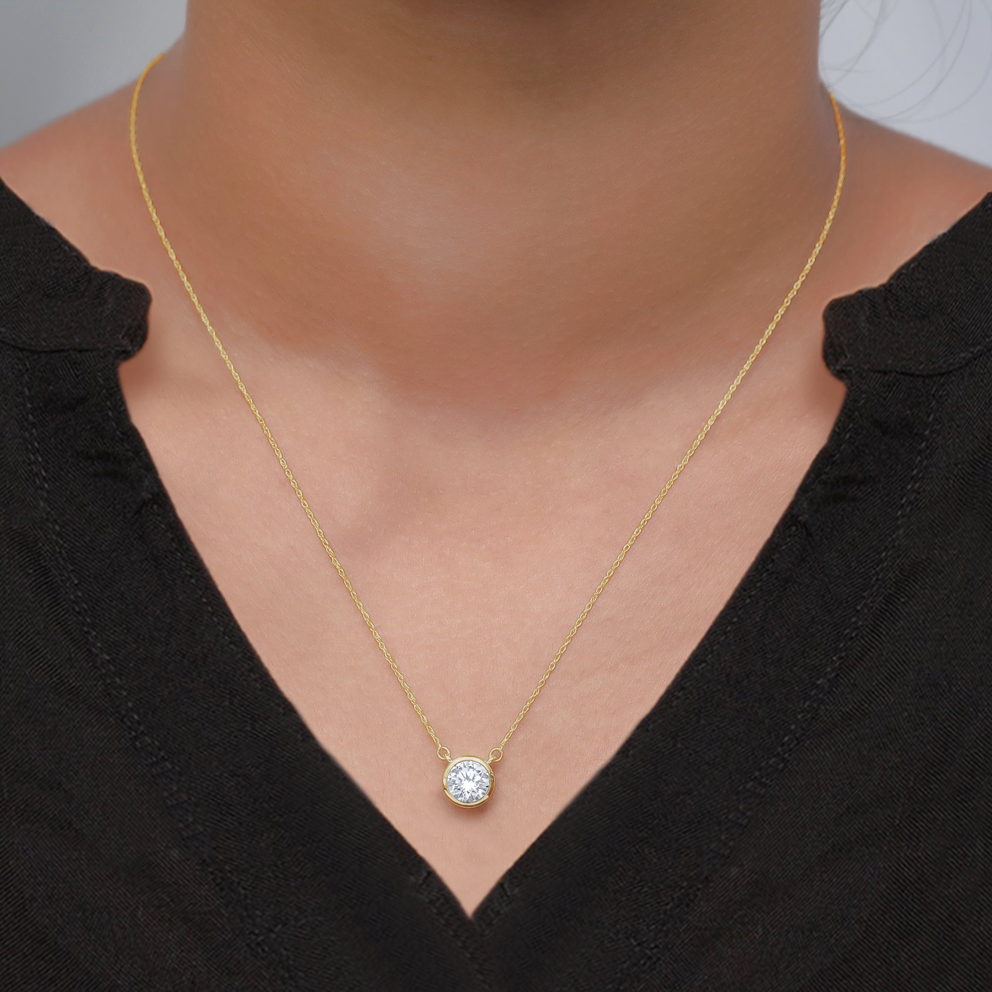 Gold necklace with a diamond pendant on a person wearing a black top.