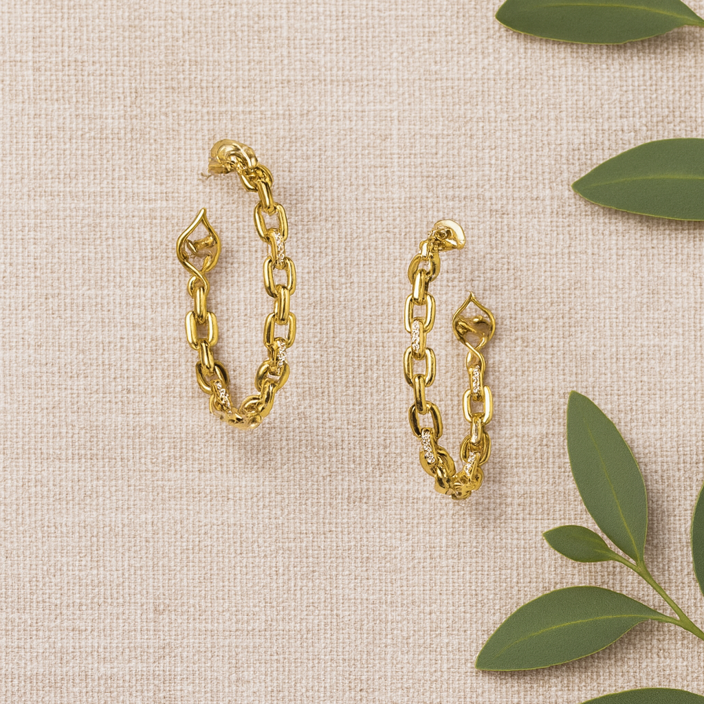 Gold chain earrings on a beige fabric background with green leaves.