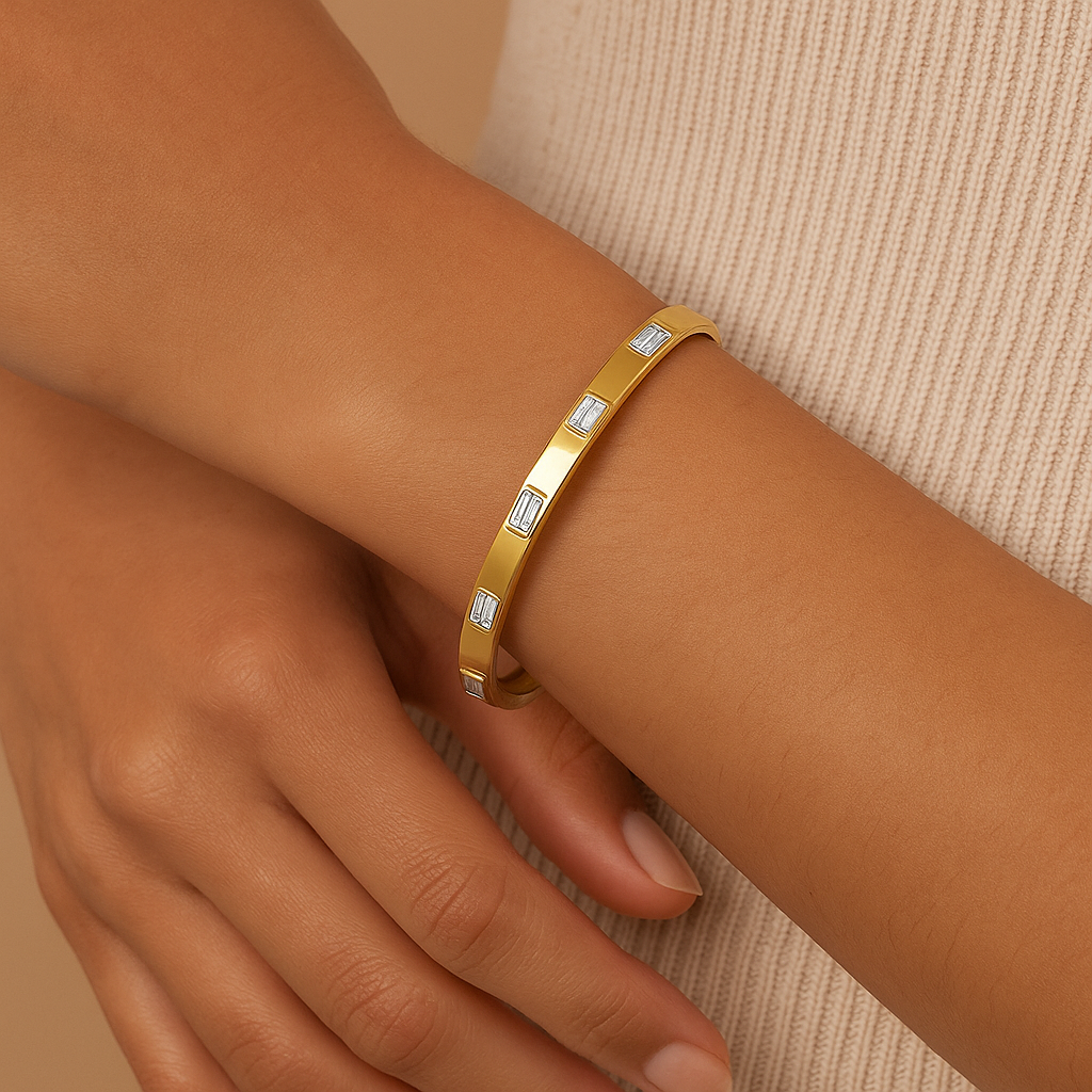 Gold bracelet with embedded stones on a wrist against a beige background
