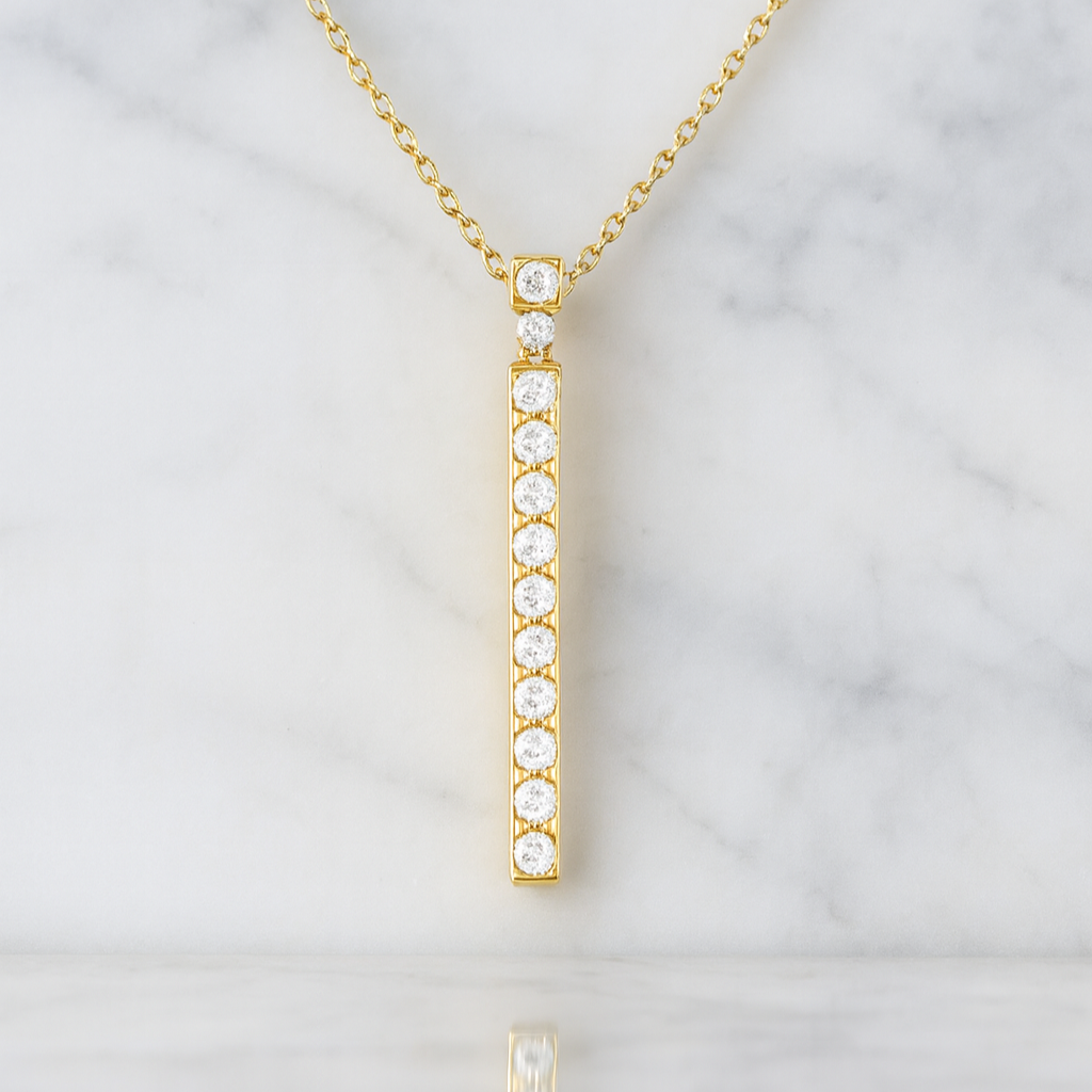 Gold necklace with a vertical diamond pendant on a marble background