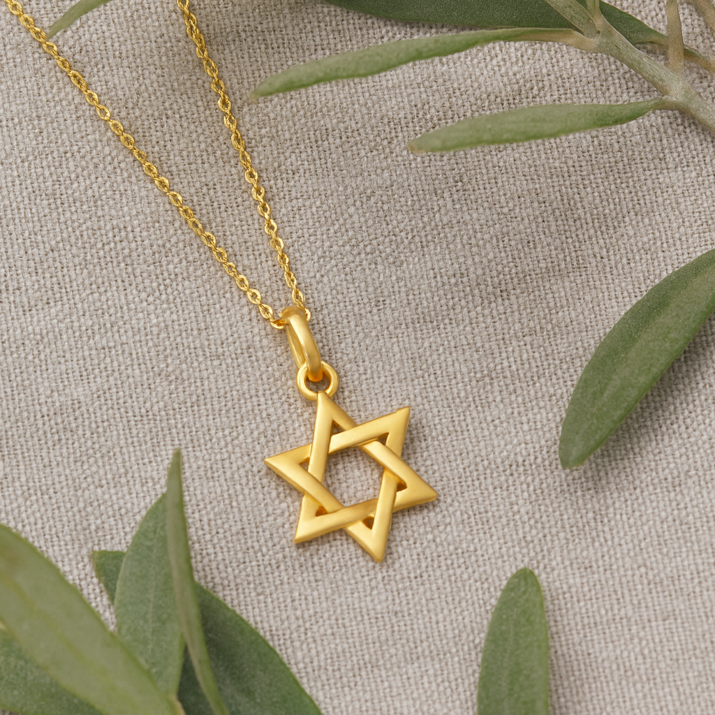 Gold Star of David necklace on a beige fabric background with green leaves.