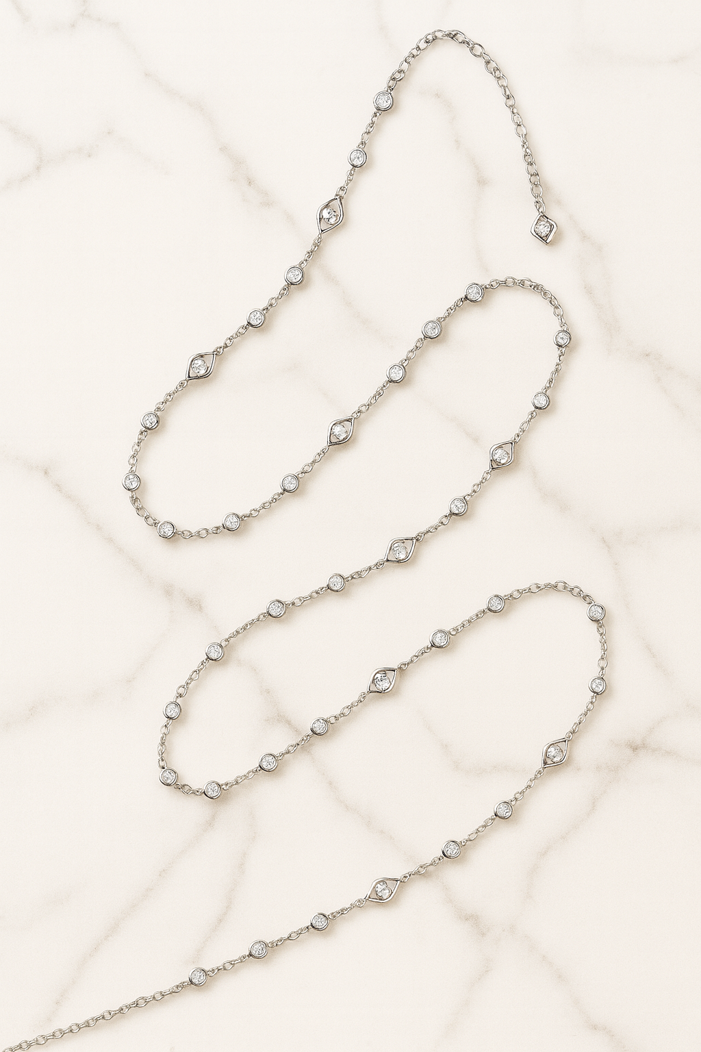 Two silver necklaces on a textured beige surface