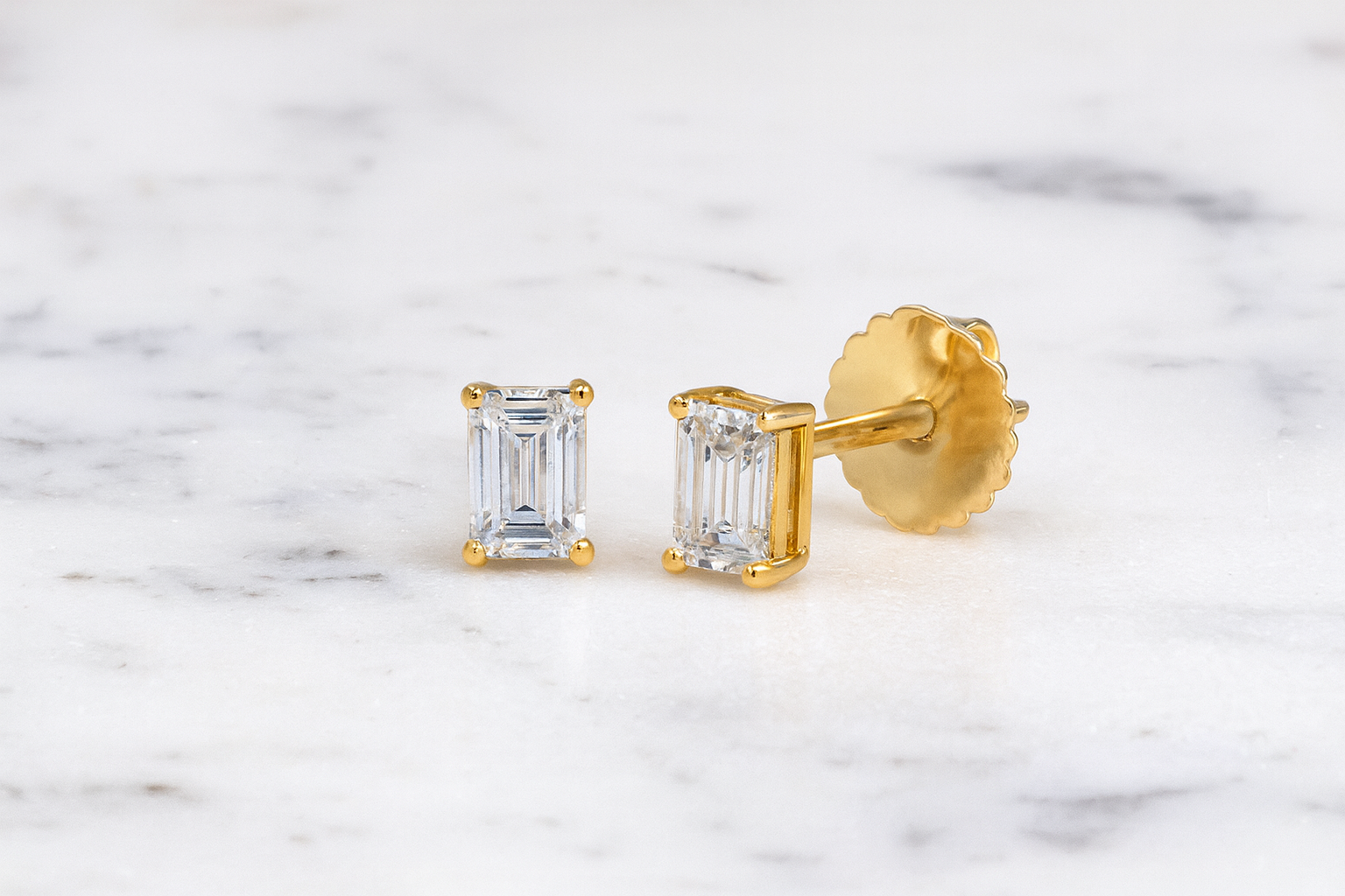 Gold earrings with emerald-cut gemstones on a marble background