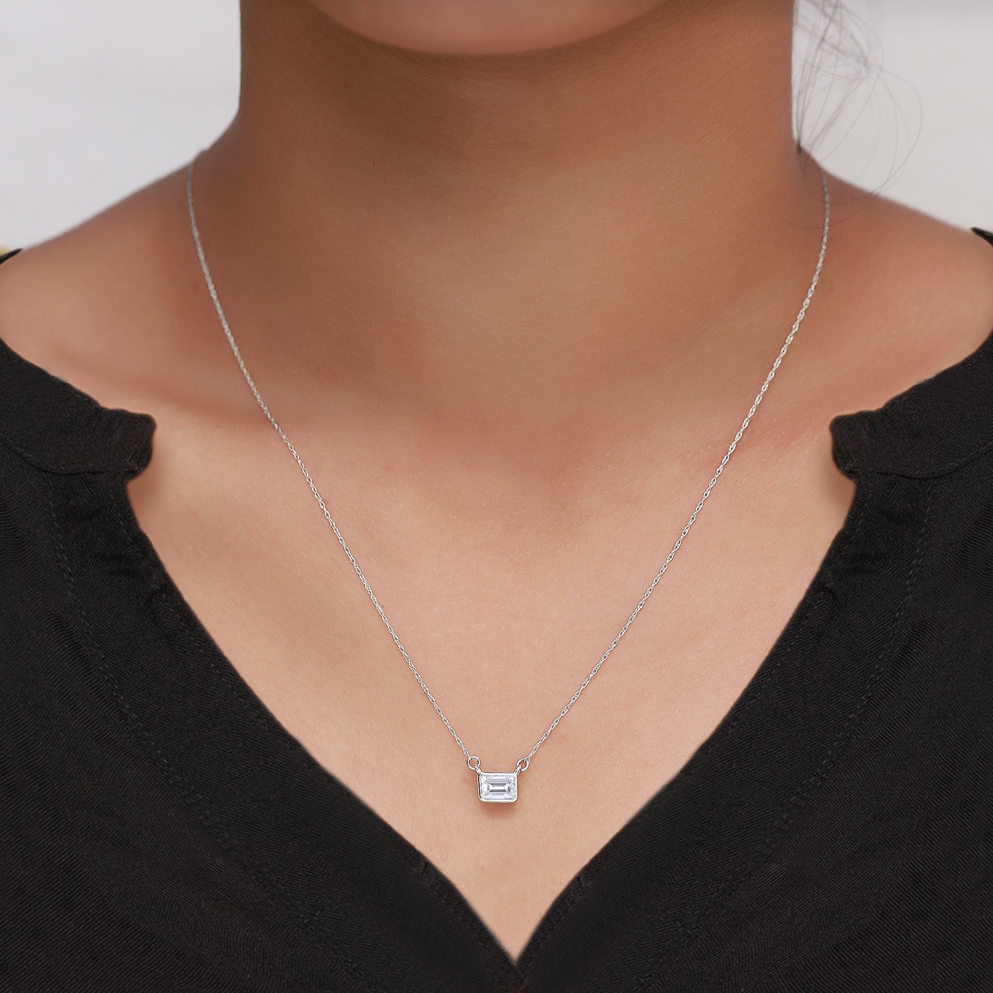Silver necklace with a small pendant on a person wearing a black top.