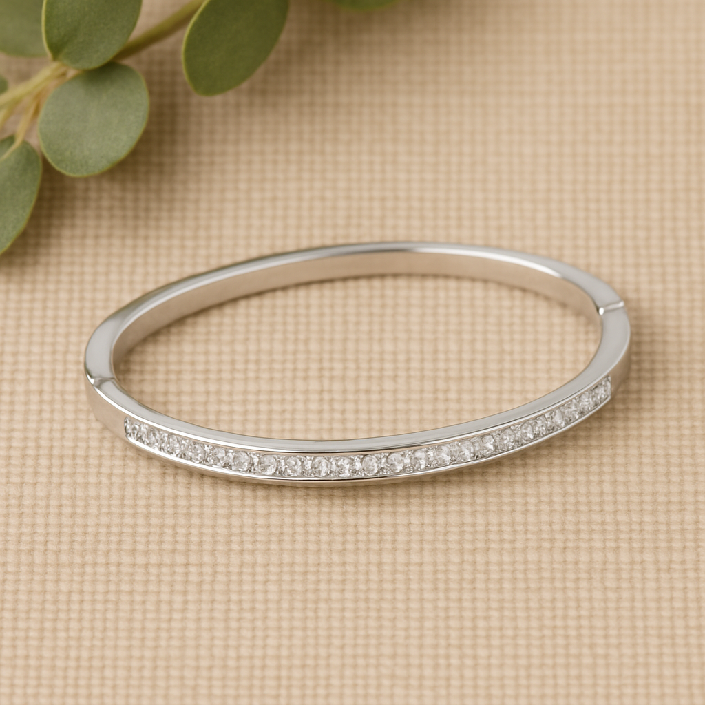 Silver bracelet with small diamonds on a beige surface with green leaves.