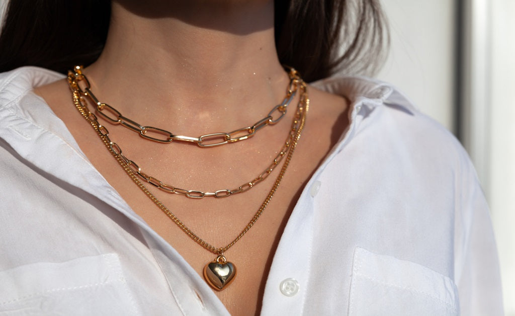 Women wearing multiple layering necklaces from a paperclip chain to a heart pendant 