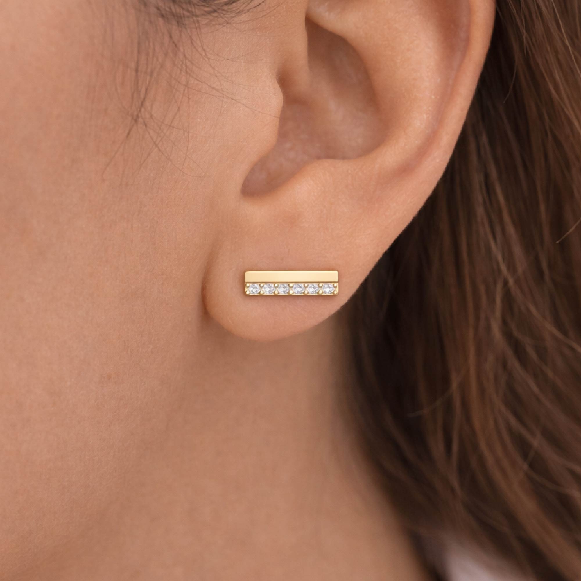 Gold bar earring with small diamonds on an ear