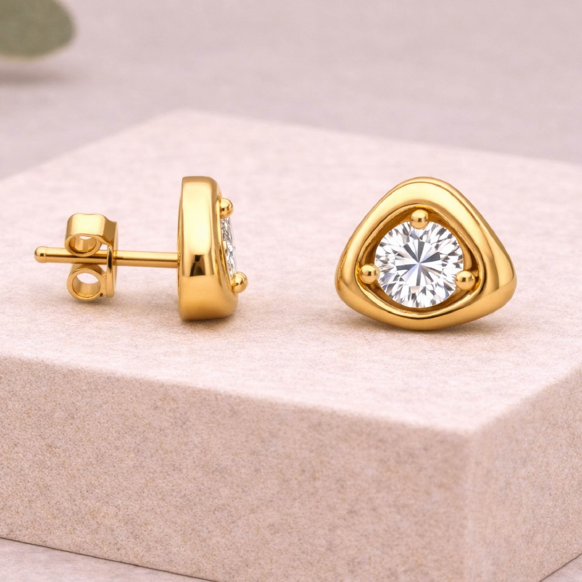 Gold earrings with clear gemstones on a beige surface