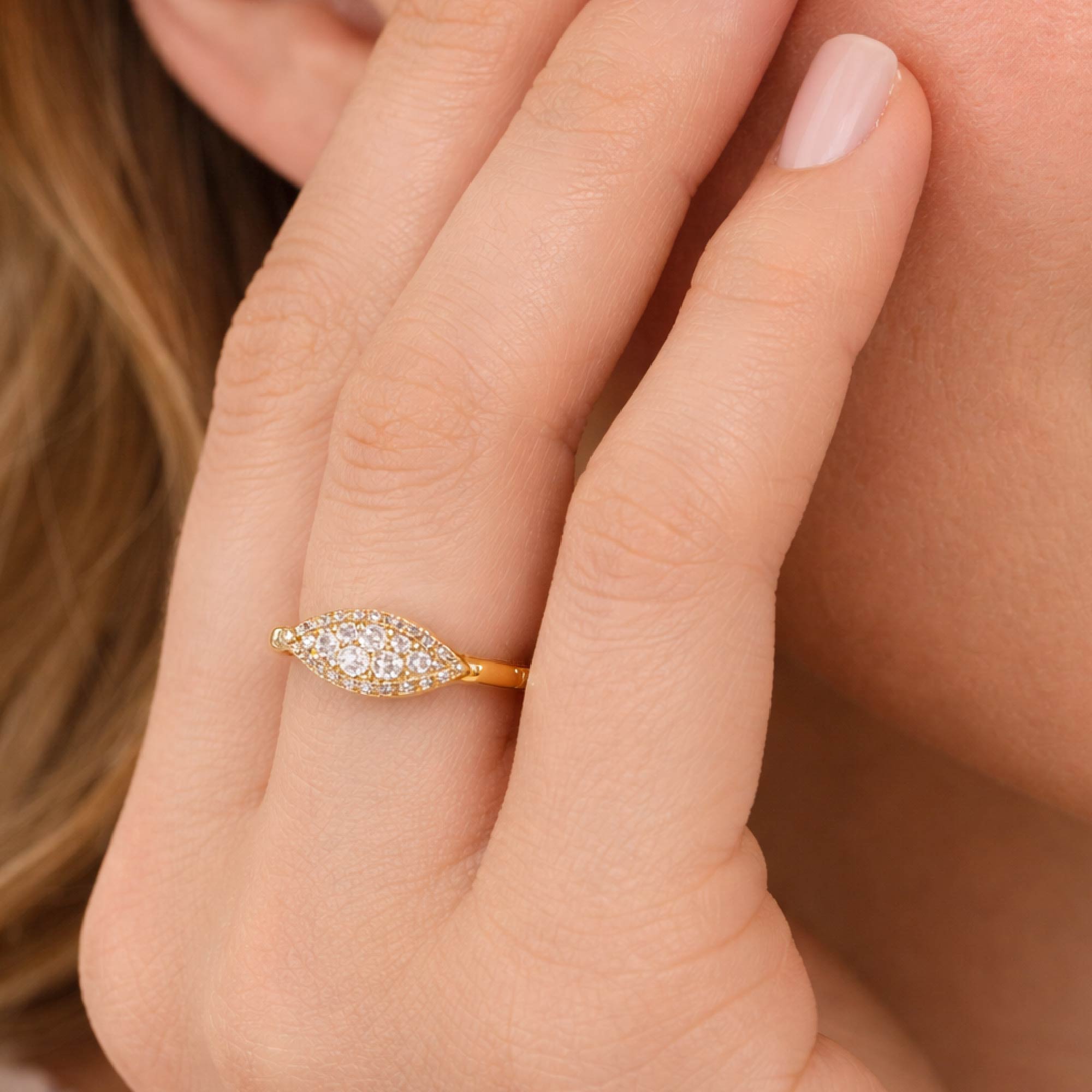 Gold ring with diamonds on a finger against a neutral background