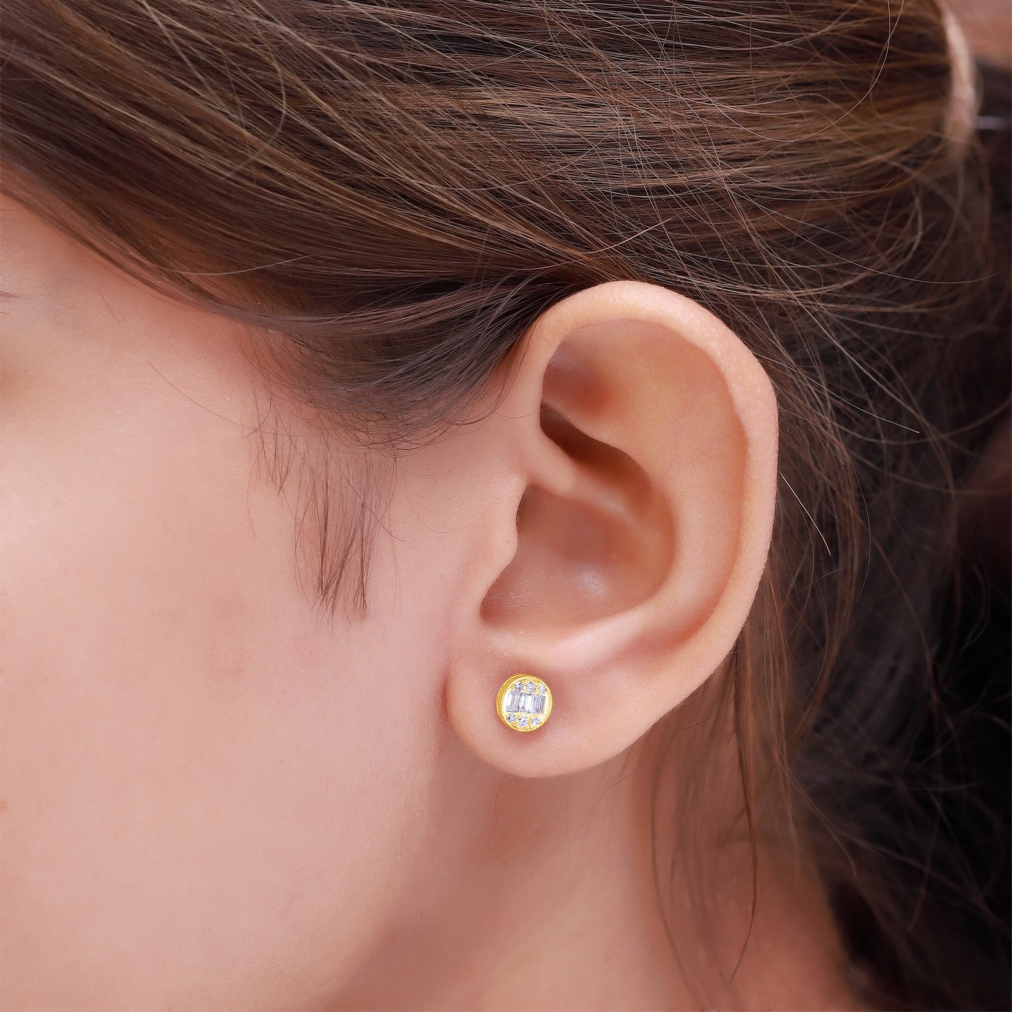 Close-up of an ear wearing a gold earring with a clear gemstone.