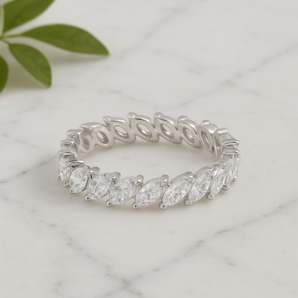 Silver ring with marquise-shaped diamonds on a marble surface with green leaves.