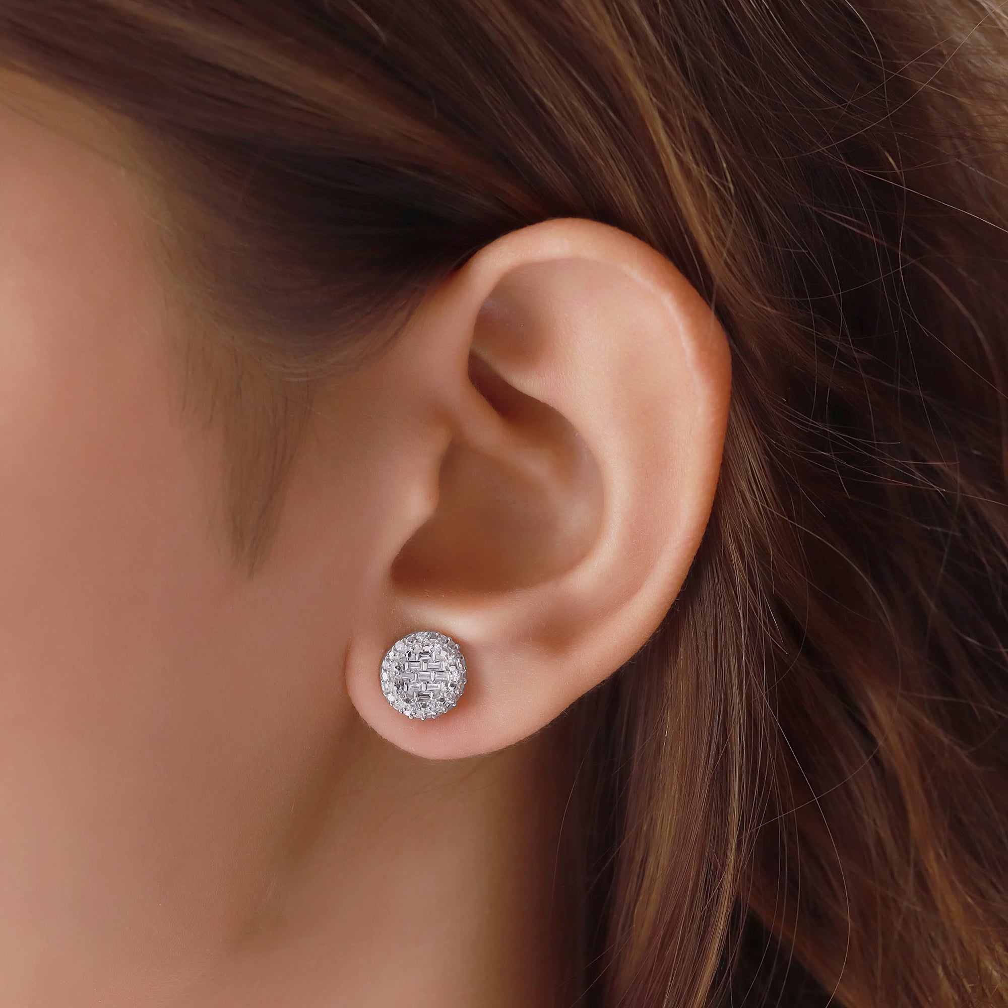 Close-up of an ear wearing a diamond stud earring with hair partially covering the frame.