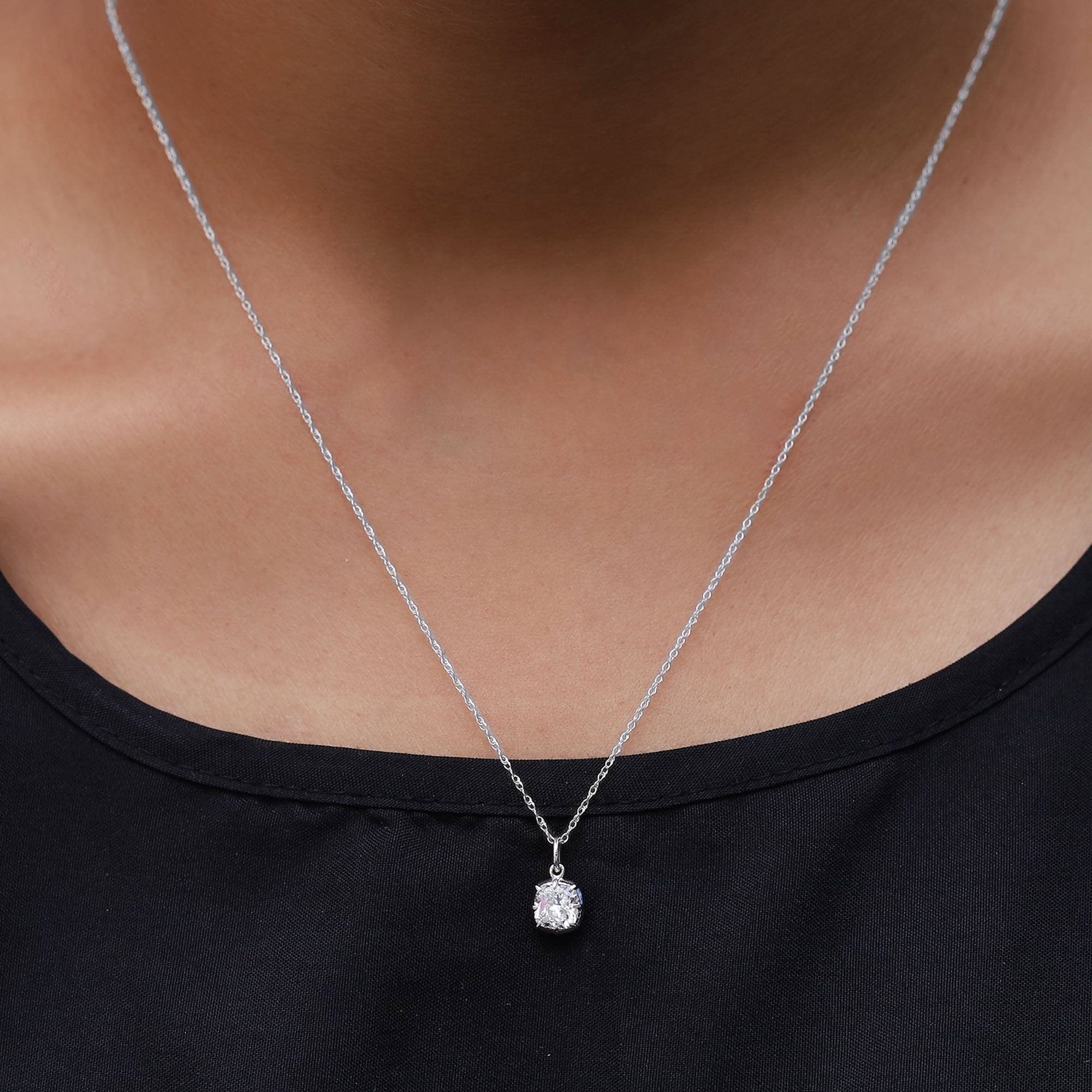 Silver necklace with a pendant worn by a person against a black background