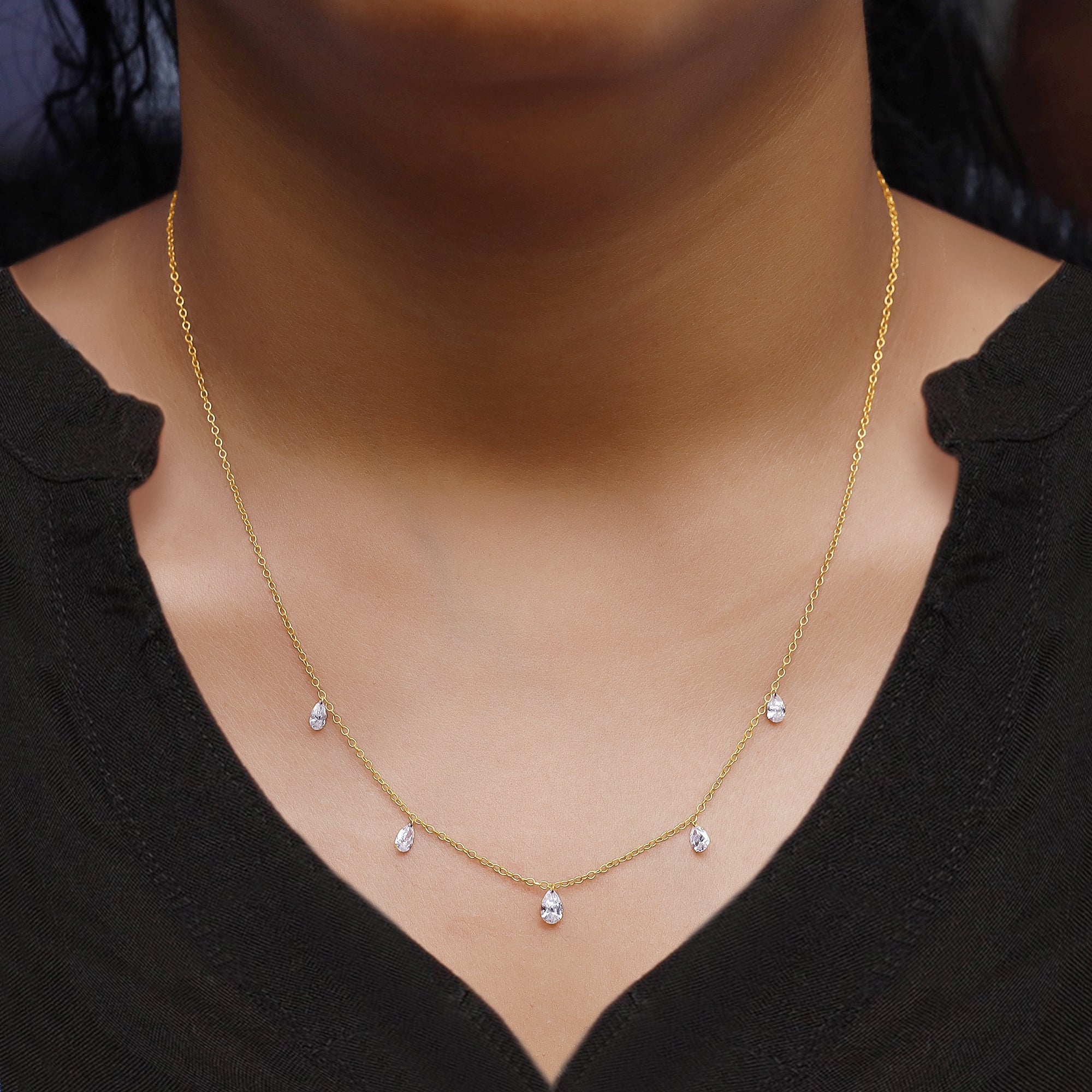 Gold necklace with small diamonds on a person wearing a black top