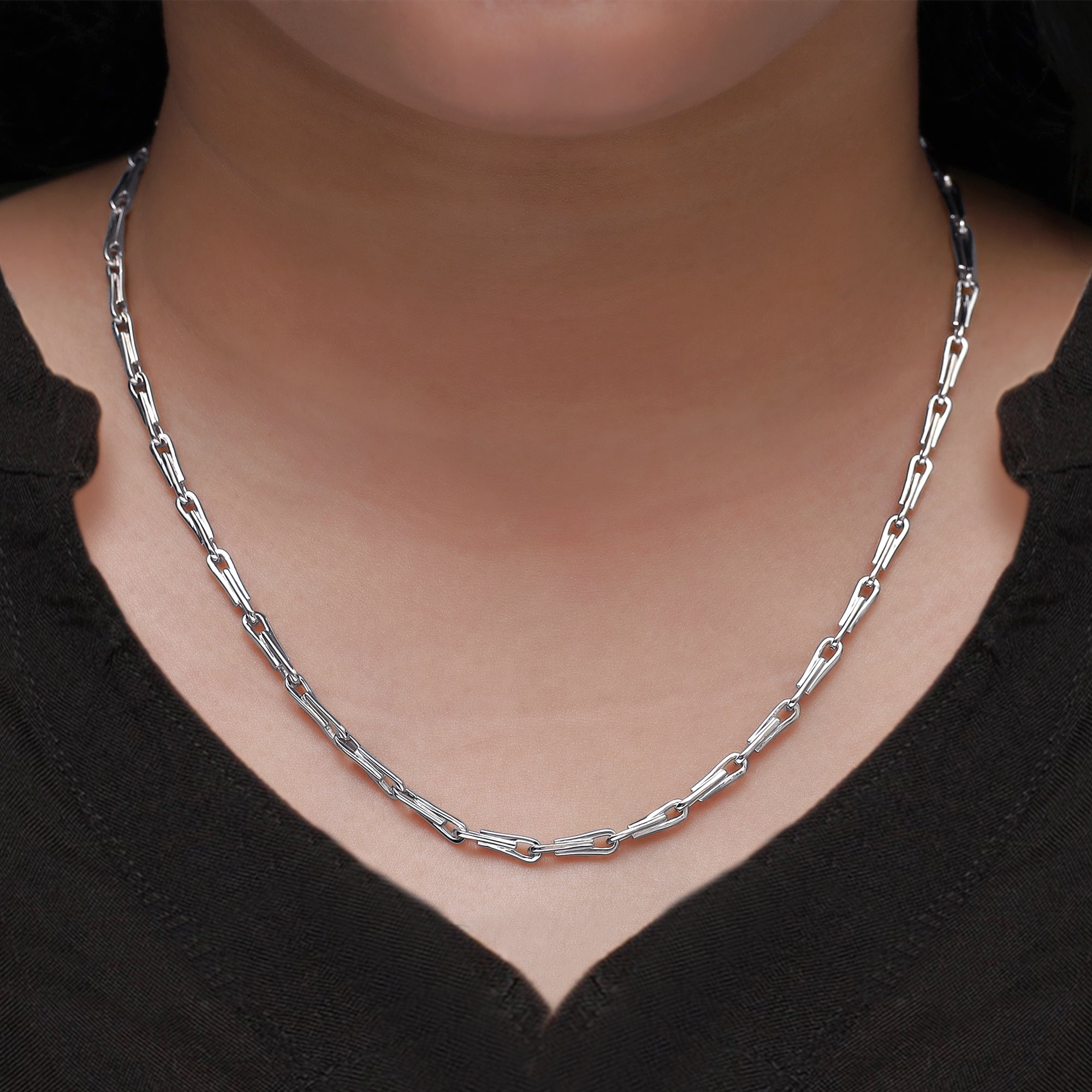 Silver chain necklace worn by a person against a black background