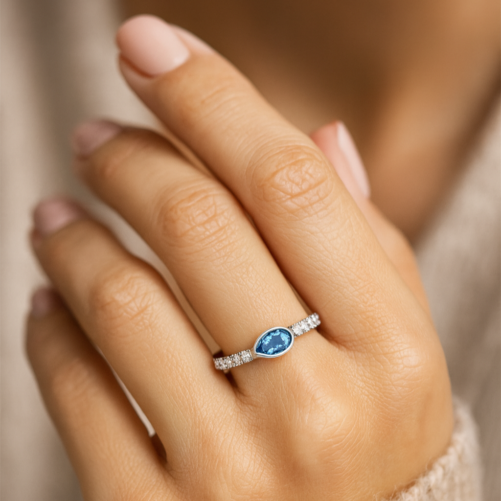 Close-up of a hand wearing a ring with a blue gemstone on a blurred background