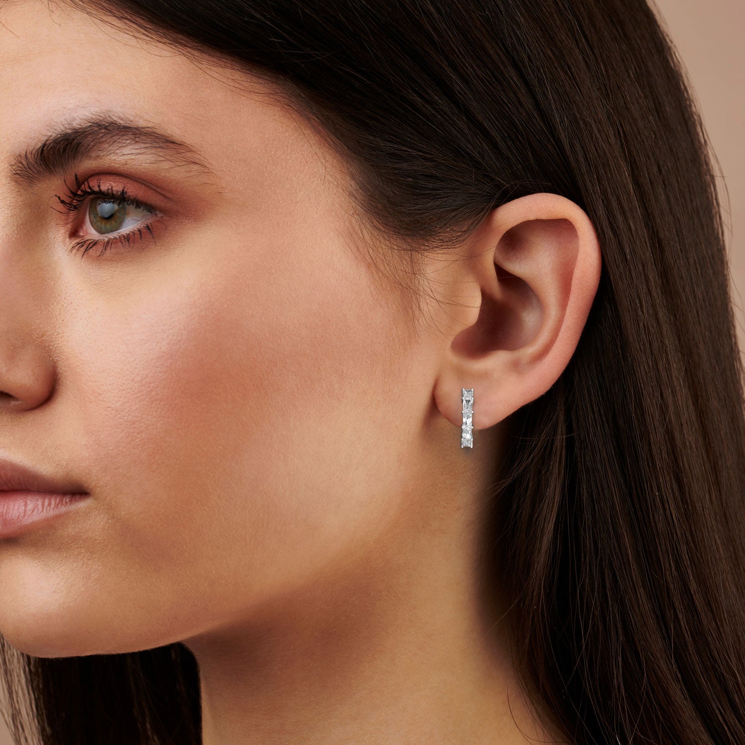 Close-up of a woman wearing a diamond earring on a neutral background