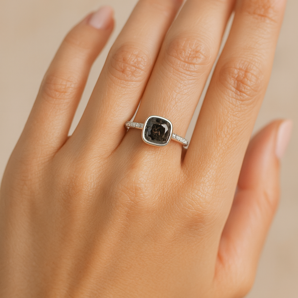 Silver ring with a dark gemstone on a hand against a beige background