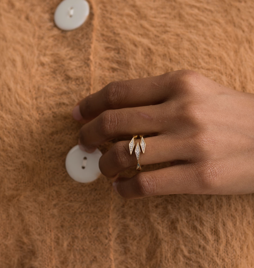 14K gold diamond ring with leaf design on hand against brown fabric