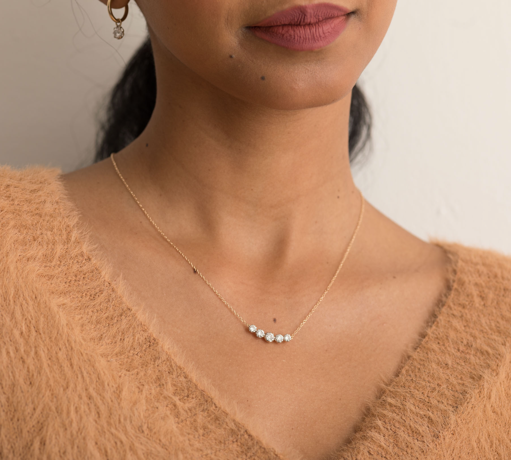 Close-up of a solid gold necklace with five diamonds on a woman's neck, worn with a beige sweater.