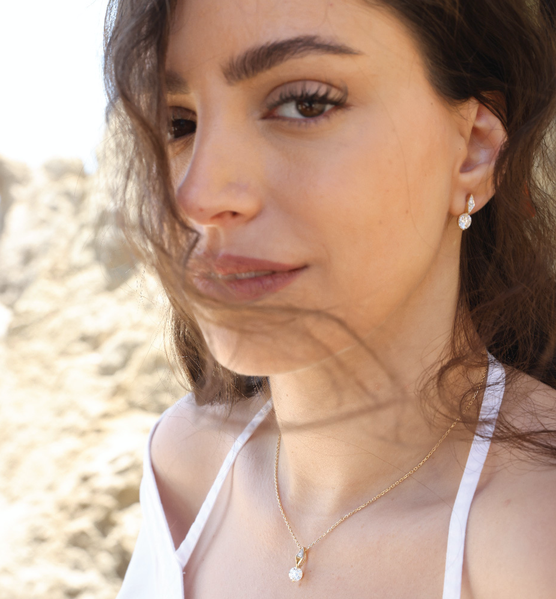 Woman wearing 14K solid gold diamond necklace and earrings with white dress outdoors.