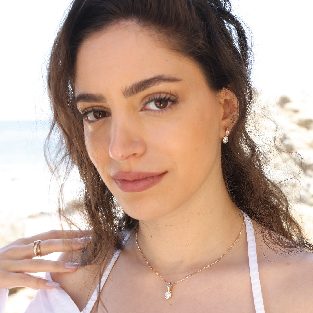 Woman wearing The Harlow 14K solid gold diamond pendant necklace with beach background.