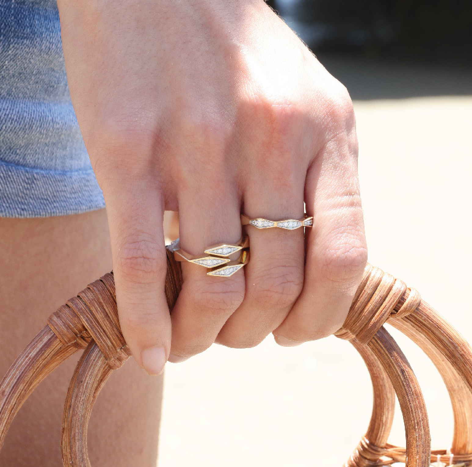 Hand wearing solid 14K gold diamond rings with intricate design on a sunny day.