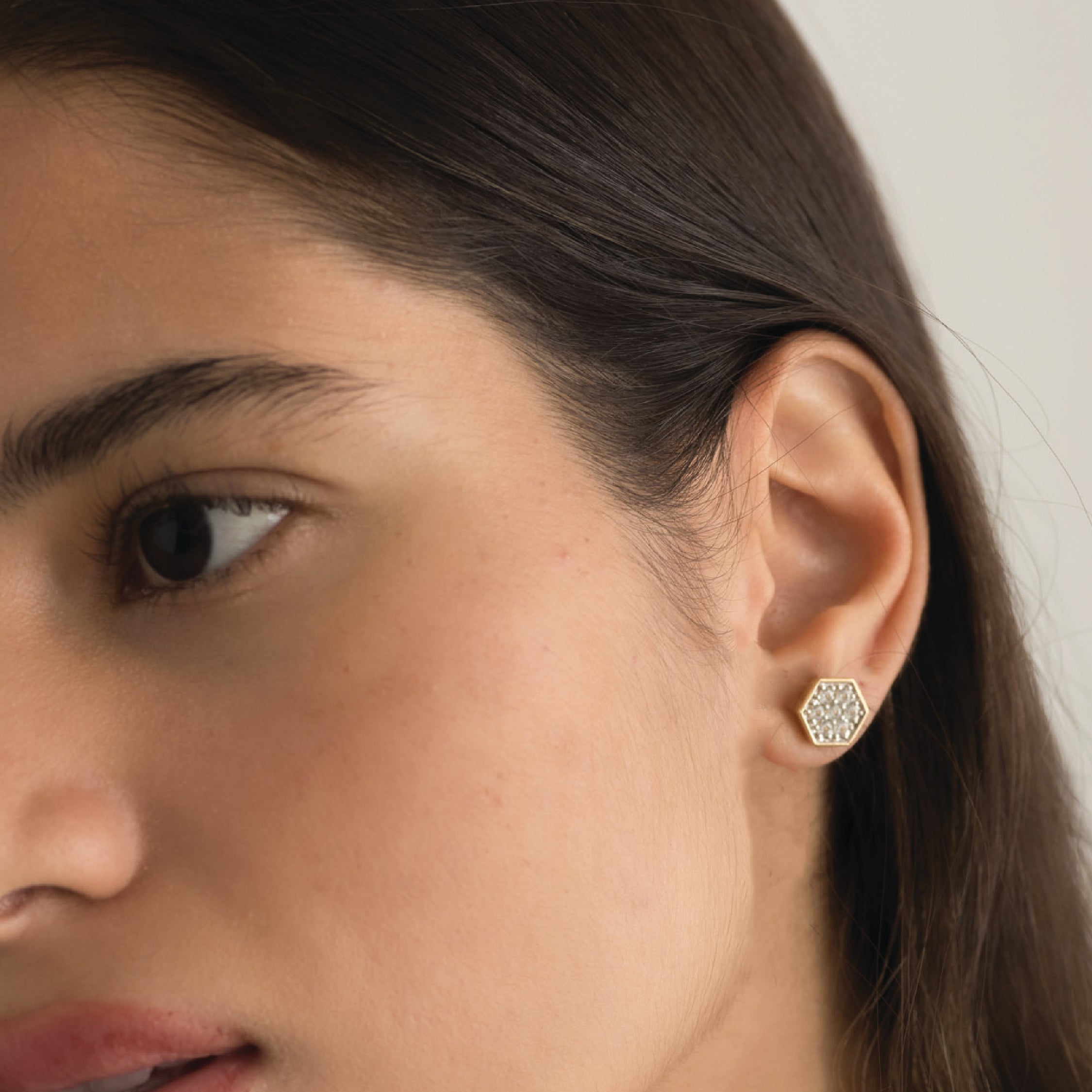Gold hexagon stud earrings with white sapphires on a woman's ear.