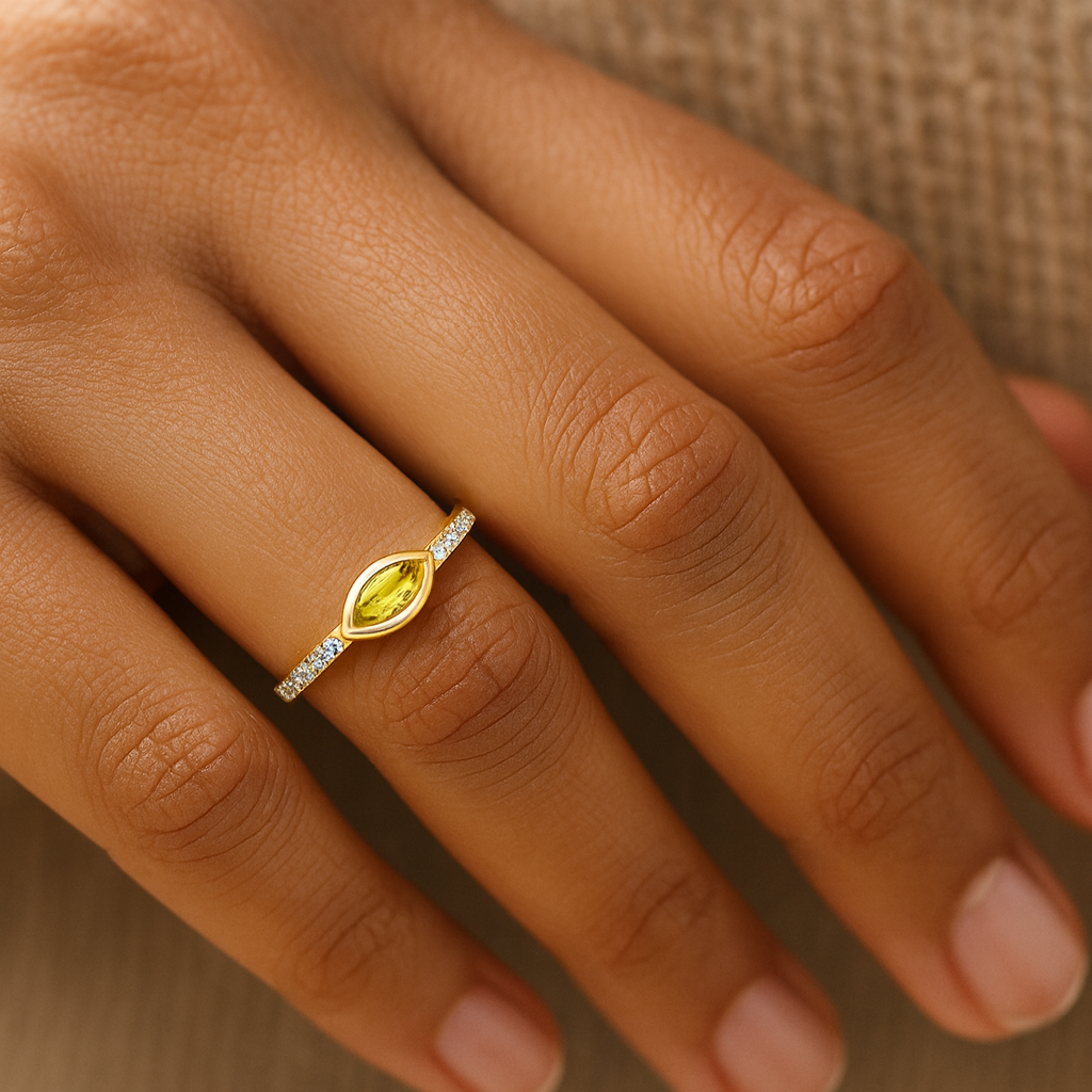 Gold ring with a yellow gemstone on a person's finger against a neutral background