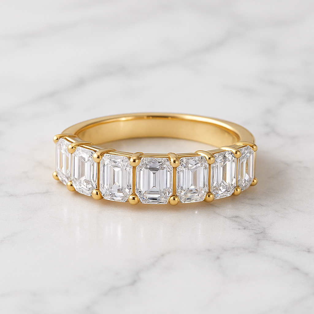 Gold ring with emerald-cut diamonds on a marble background