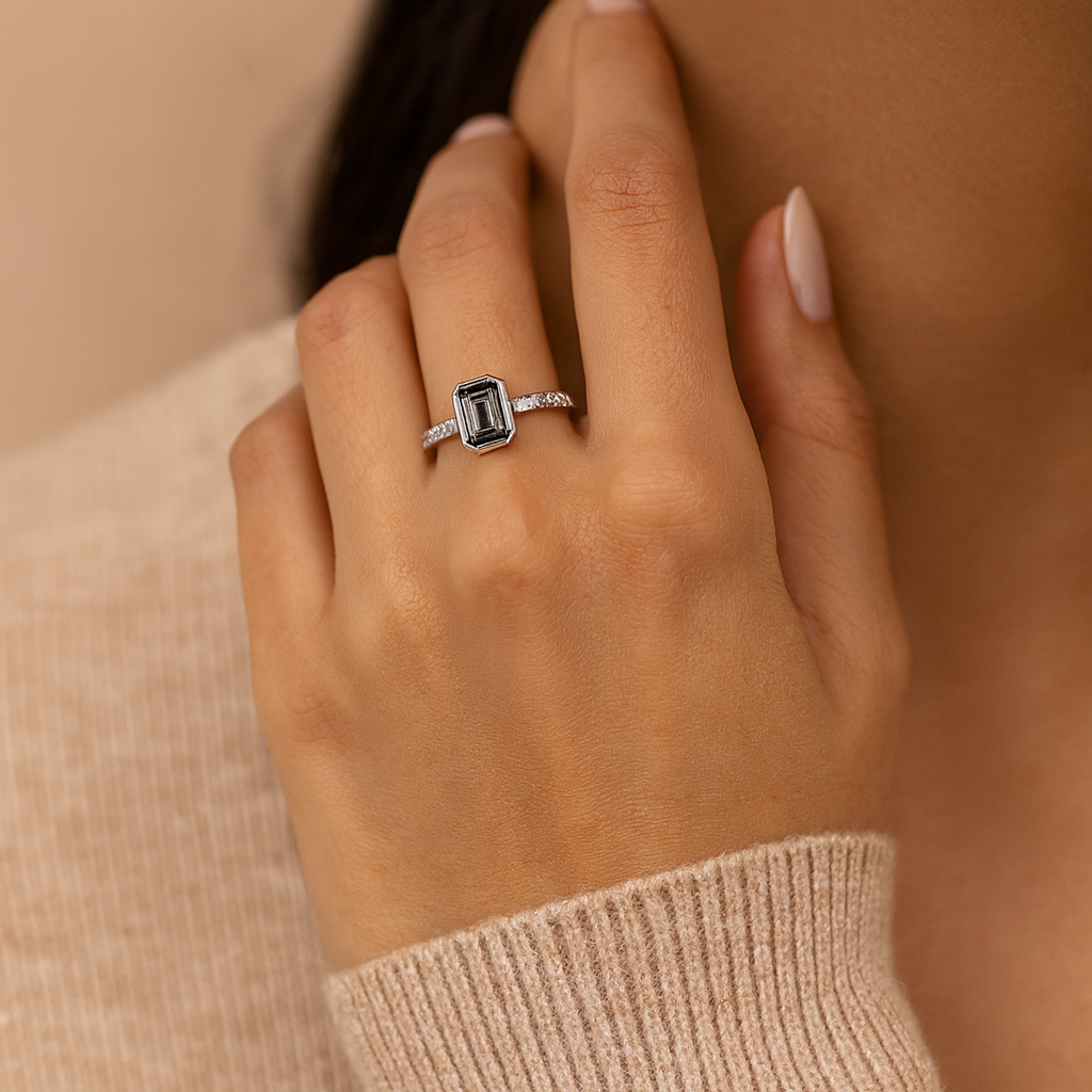 Hand wearing a silver ring with a green gemstone against a neutral background