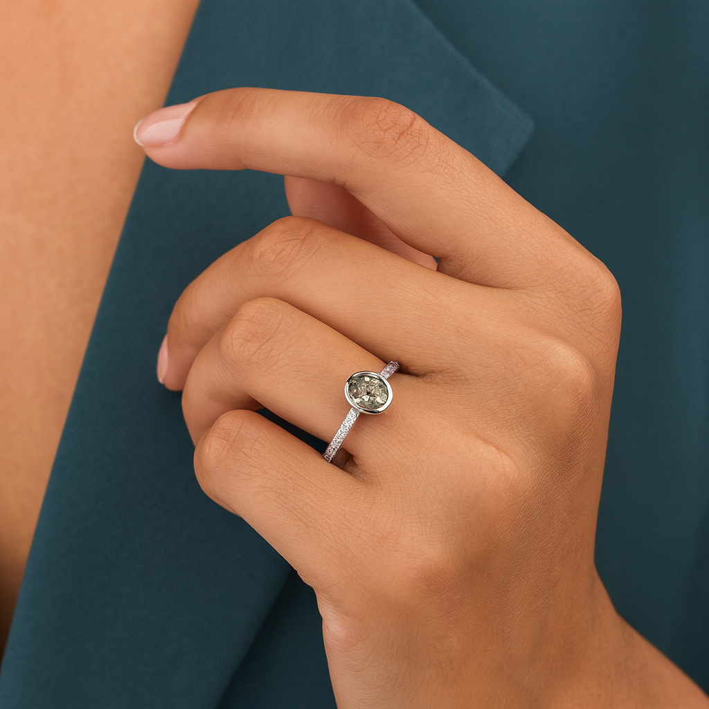 Close-up of a hand wearing a silver ring with a green gemstone against a teal background