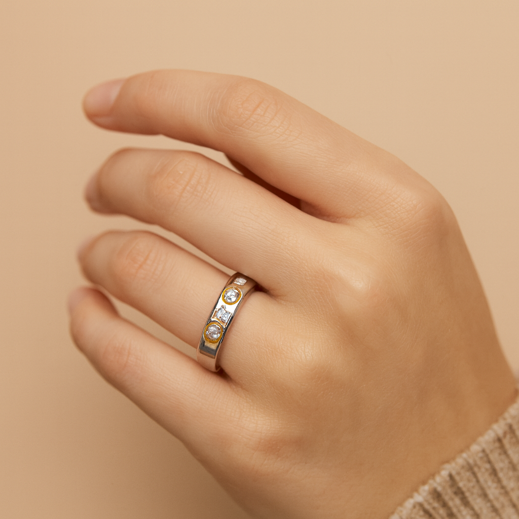 Hand wearing a silver ring with small stones on a beige background