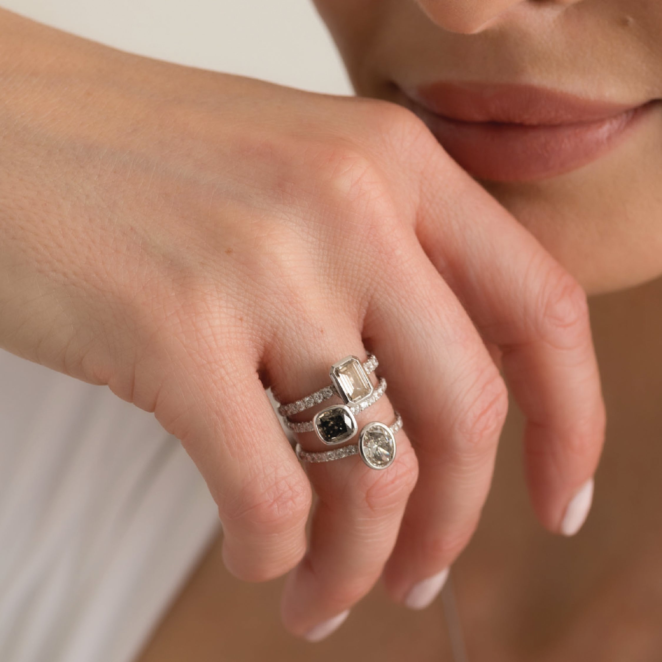 Hand wearing three white gold rings with smokey diamonds in various shapes.